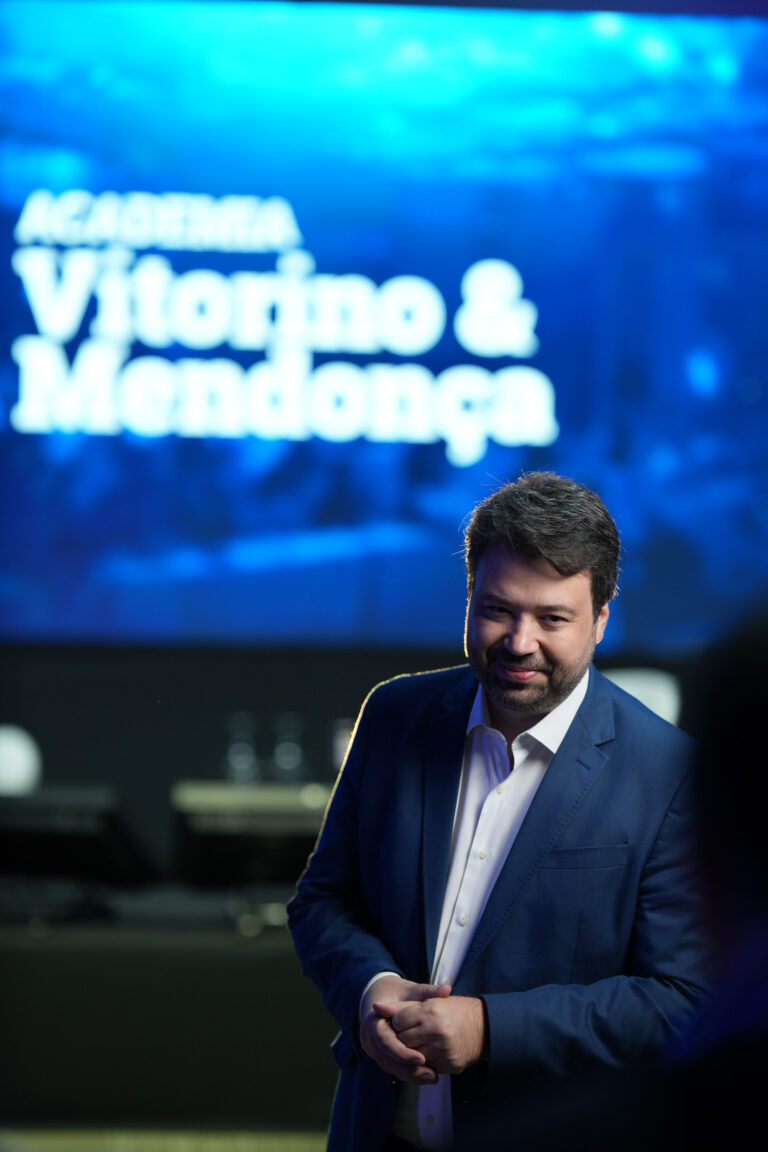 Marcelo Vitorino sorri em evento da Academia Vitorino & Mendonça, com a marca projetada ao fundo