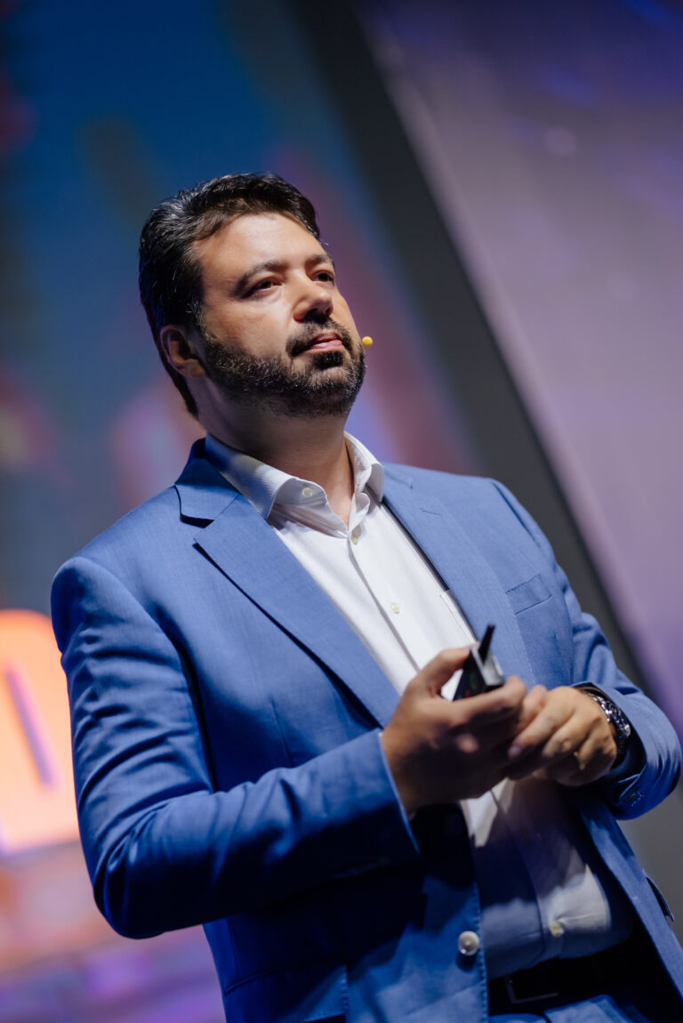 Marcelo Vitorino, de blazer azul, durante palestra no palco, com microfone