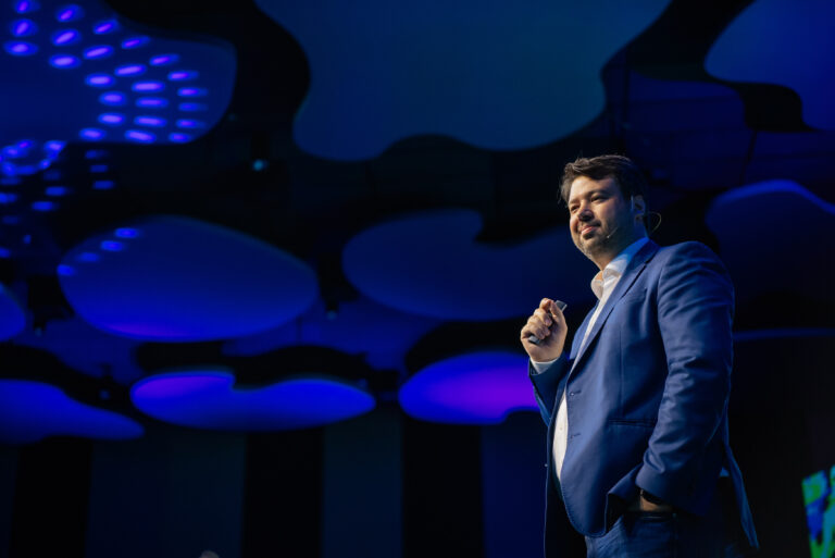 Marcelo Vitorino no palco durante palestra, sob iluminação azul