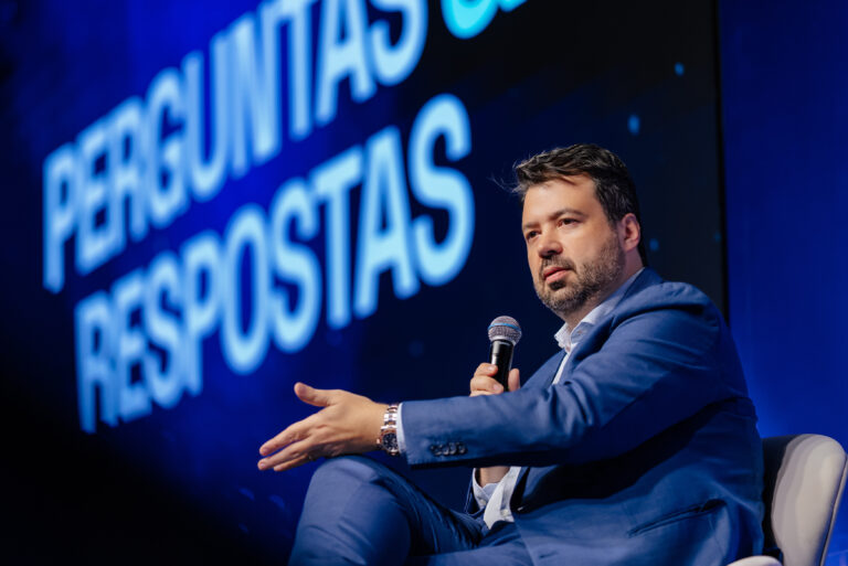 Marcelo Vitorino responde a perguntas do público com o microfone na mão, diante do telão de perguntas e respostas
