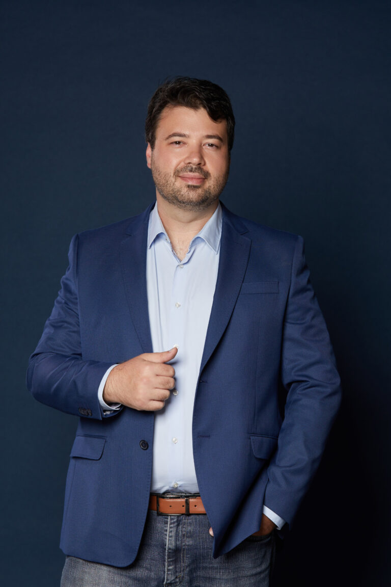 Retrato de estúdio de Marcelo Vitorino, de blazer azul-marinho sobre camisa azul-clara